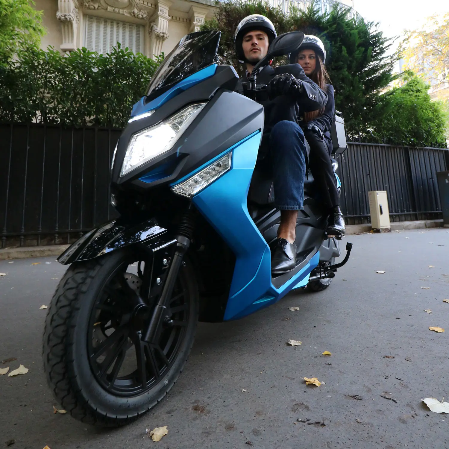 pink-fly-couple-parking Scooter électrique Pink Mobility Pink Fly Phase 3 bleu en circulation avec deux passagers, en milieu urbain.